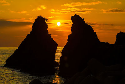 Silhouette rocks on shore against sky during sunset