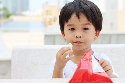 Asian boy sitting on a concrete chair and eating a snack.