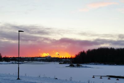 Snow covered field against sky during sunset