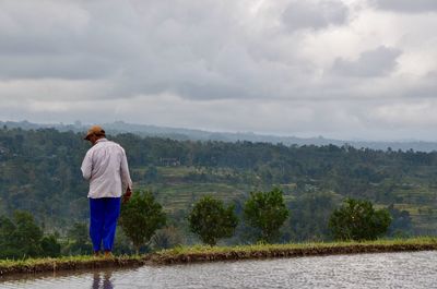 Rear view of man standing on mountain against sky