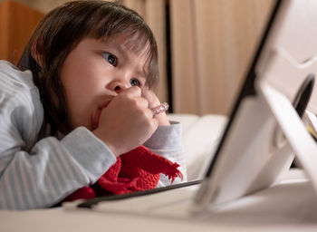 Close-up of cute girl sucking thumb while using digital tablet at home