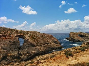 Man standing on cliff by sea against sky