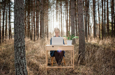 Travelling woman working on a laptop and desk in a peaceful forest