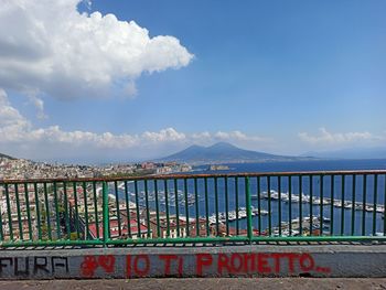 Graffiti on railing by sea against blue sky