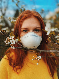 Close-up portrait of young woman wearing mask amidst flowers