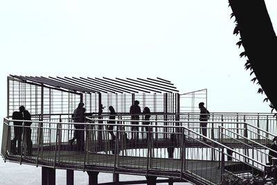 Silhouette people standing by railing against clear sky