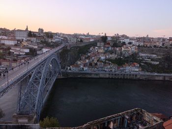 Bridge over river by buildings in city against sky during sunset