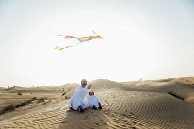 Rear view of women sitting on sand against sky