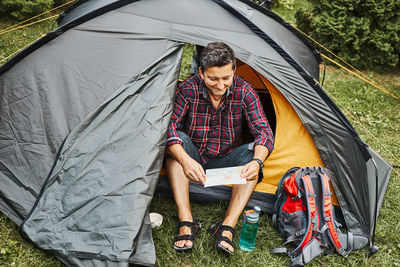 Man looking at map while planning next trip. man relaxing in tent at camping. concept of camp life