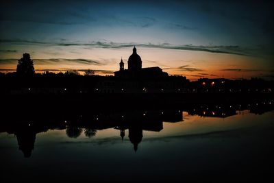 Silhouette church by calm lake against sky at dusk