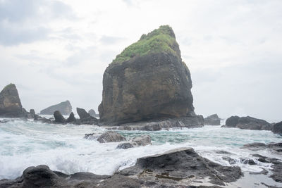 Rock formation in sea against cloudy sky