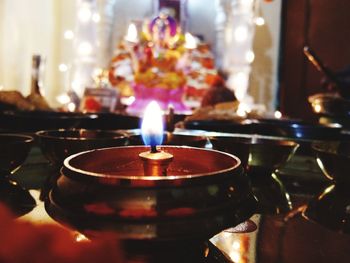 Close-up of illuminated diya against ganesha in temple