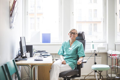 Portrait of smiling mature female doctor sitting in clinic