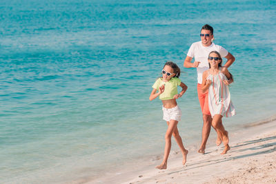 Full length of father and daughters running on beach