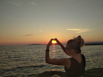 Woman standing by sea against sky during sunset