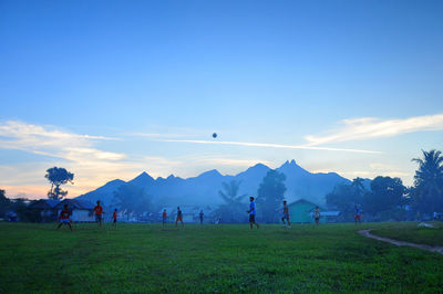 Men playing soccer on grassy field against sky