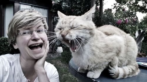 Portrait of woman making face by cat against trees