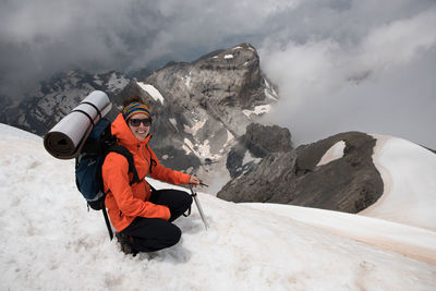 Side view portrait of smiling backpacker crouching on snowcapped mountain during winter