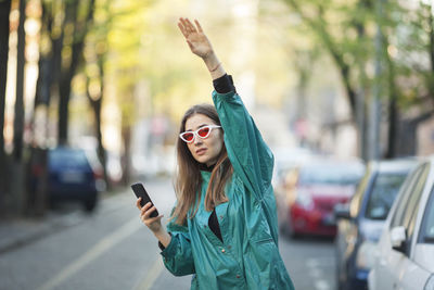 Portrait of woman hailing ride and holding mobile phone while standing in city