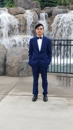 Full length portrait of young man standing against waterfall