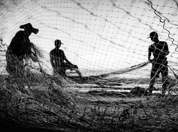 Fishermen holding net at shore against sky