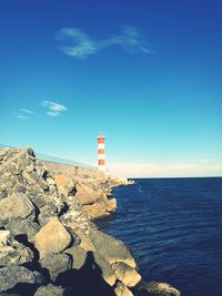 Lighthouse by sea against blue sky