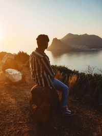 Man sitting on rock by mountain against sky