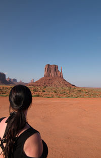 Rear view of woman standing on rock against clear sky