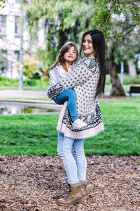 Portrait of smiling mother carrying cute daughter while standing in park