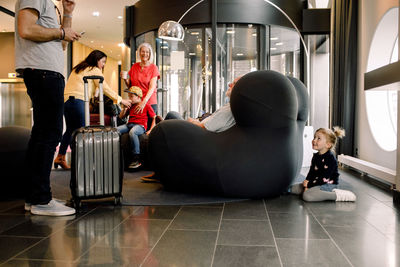 Smiling girl hiding against armchair with family having drink while sitting in hotel lobby