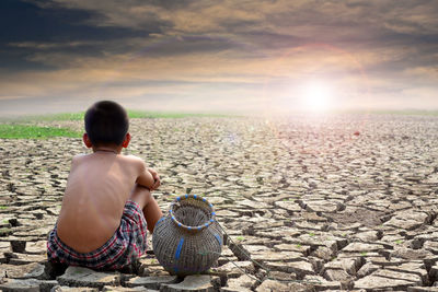 Rear view of boy sitting on barren land against sky