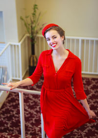 Portrait of smiling woman in red dress standing at home