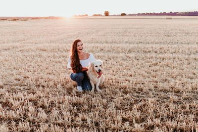 Woman with dog on field against sky during sunset