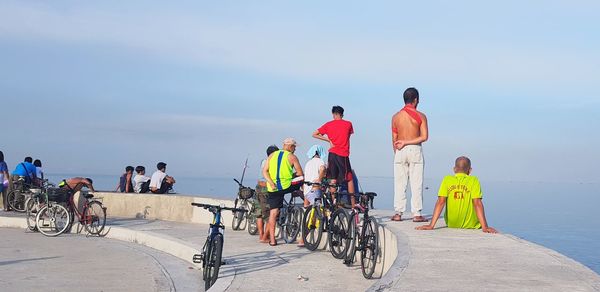 Rear view of people riding bicycle by sea against sky