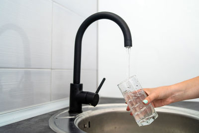 Cropped hand of woman filling water in glass from faucet