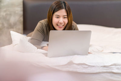 Young woman using phone while relaxing on bed