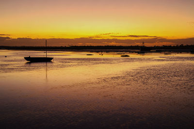 Silhouette boats moored on sea against orange sky