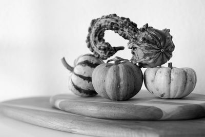 A selection of mini pumpkin decorations standing on a wooden chopping board monochrome