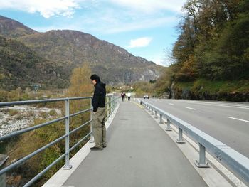 Side view of man standing on bridge against mountains