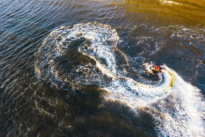 Aerial view of young man making infinite loop riding on fast water scooter on sunset in golden water