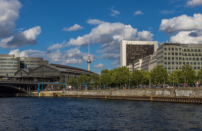 View of buildings by river against cloudy sky during sunny day