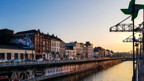 Bridge over river by buildings against sky at sunset