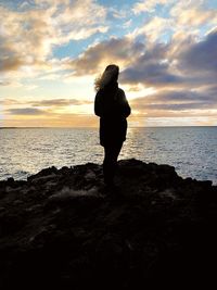 Silhouette woman standing at beach against sky during sunset