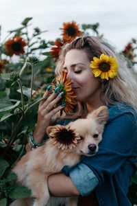 Woman carrying dog while smelling sunflower at farm