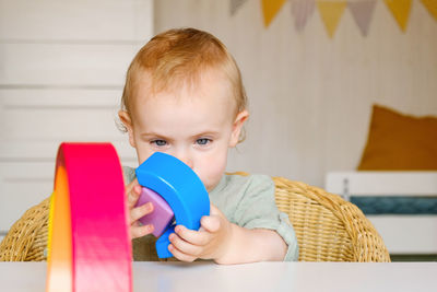 Little baby child in clothes made of natural fabric plays with rainbow colored wooden toys at white