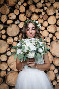 Young woman holding flower bouquet standing against logs