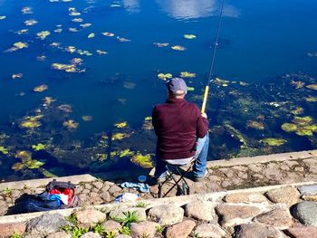 Rear view of man sitting on rock by lake