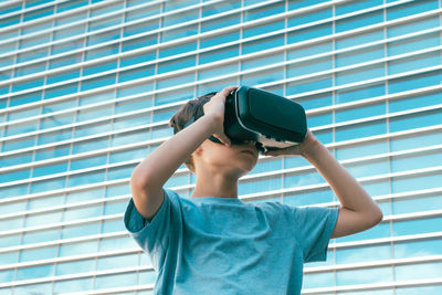 Low angle view of boy using virtual reality simulator against building