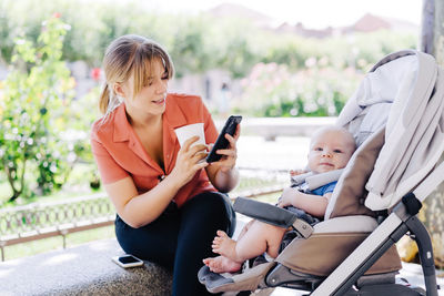 Portrait of young mother with her baby in a child carrier drinking a coffee while