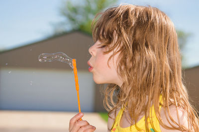 Close-up of girl blowing bubble against sky